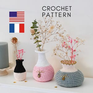 Könnte beinhalten: Drei gehäkelte Vasen in verschiedenen Farben und Größen. Die kleinste Vase ist schwarz-weiß, die mittlere Vase ist weiß-rosa und die größte Vase ist grau-weiß. Jede Vase hat einen kleinen Anhänger. Die Vasen sind mit Trockenblumen gefüllt.