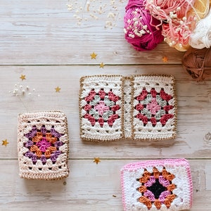 Puede incluir: Tres cuadrados de granny crochet en rosa, blanco y naranja con ribete dorado. Los cuadrados est&aacute;n sobre una superficie de madera blanca con estrellas doradas.