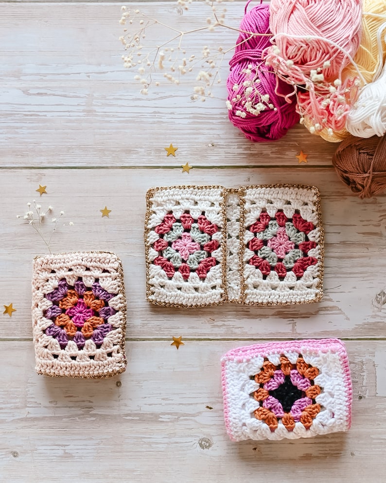 Puede incluir: Tres cuadrados de granny crochet en rosa, blanco y naranja con ribete dorado. Los cuadrados est&aacute;n sobre una superficie de madera blanca con estrellas doradas.