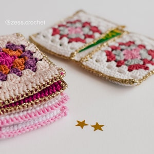 Puede incluir: Una pila de cuadrados de ganchillo rosa y blanco con ribetes dorados, y dos estrellas doradas sobre una superficie blanca. El texto '@zess.crochet' es visible en la esquina superior izquierda de la imagen.