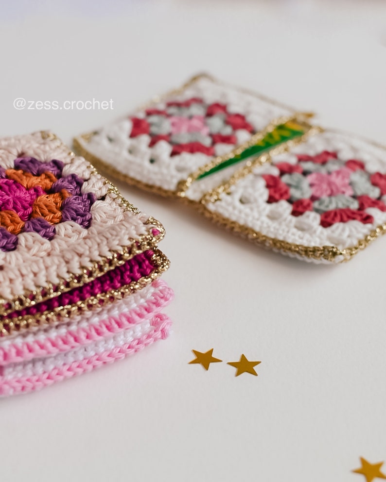 Puede incluir: Una pila de cuadrados de ganchillo rosa y blanco con ribetes dorados, y dos estrellas doradas sobre una superficie blanca. El texto '@zess.crochet' es visible en la esquina superior izquierda de la imagen.