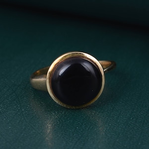 May include: A gold ring with a black oval gemstone set in a bezel setting.