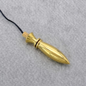 Op de afbeelding: Een gouden slinger met een puntige punt en een zwart touwtje dat aan de bovenkant is bevestigd.