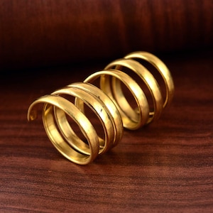 May include: A gold-toned metal ring with a spiral design. The ring is made of multiple bands that are intertwined to create a unique and intricate look.
