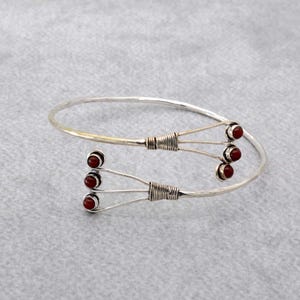 May include: Silver bangle bracelet with three branches of red gemstone accents.