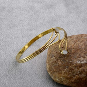 May include: A gold bangle bracelet with two white stones. The bracelet has a delicate, flowing design.
