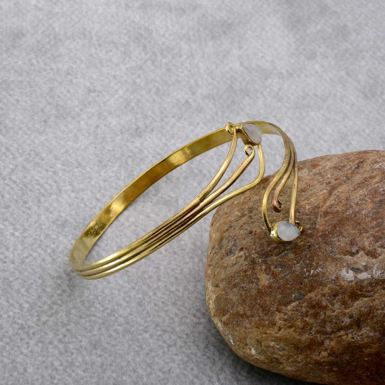 May include: A gold bangle bracelet with two white stones. The bracelet has a delicate, flowing design.