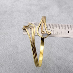 May include: Gold-tone bracelet with two white stones, measured against a ruler. The bracelet is approximately 2 inches in diameter.