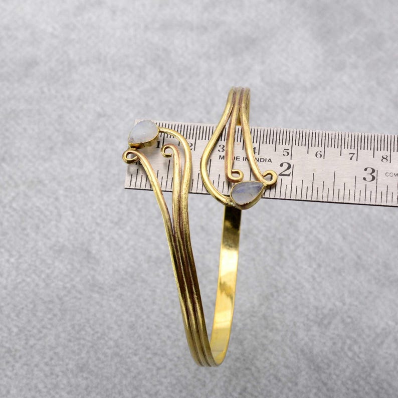 May include: Gold-tone bracelet with two white stones, measured against a ruler. The bracelet is approximately 2 inches in diameter.