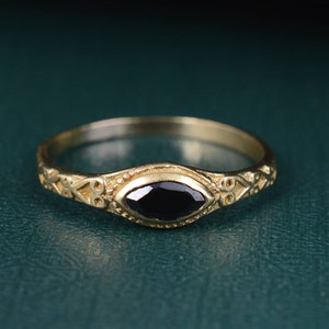Puede incluir: Un anillo de oro con una piedra preciosa negra ovalada engastada en un diseño ornamentado y detallado.