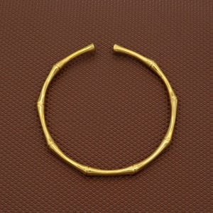 Op de afbeelding: Een gouden armband met een bamboe-geïnspireerd ontwerp. De armband is gemaakt van een reeks verbonden, afgeronde segmenten die lijken op bamboestokken.