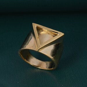 May include: A gold-toned ring with a triangular design. The ring is made of metal and has a smooth, polished finish.