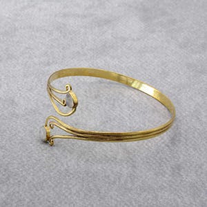 May include: A gold-toned bangle bracelet with two white oval-shaped stones. The bracelet is open and has a delicate, intricate design.