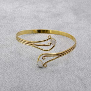 May include: A gold-tone bangle bracelet with two white stones set in the design. The bracelet is made of twisted metal and has a delicate, feminine look.