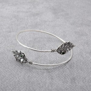 Op de afbeelding: Zilveren armband met twee blaadjesvormige bedels, elk met een groene edelsteen in het midden.