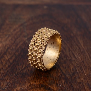 Peut inclure: Une bague en or avec un motif texturé de petits cercles en relief. La bague est en métal brillant et a une finition lisse et polie.