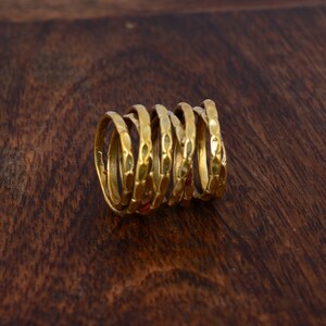 May include: A stack of six gold-colored rings with a textured design. The rings are stacked on top of each other and are arranged in a spiral shape.