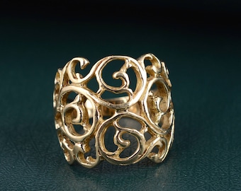 Puede incluir: Un anillo de filigrana dorado con un diseño delicado e intrincado. El anillo está hecho de una sola pieza de metal y tiene una banda ancha.