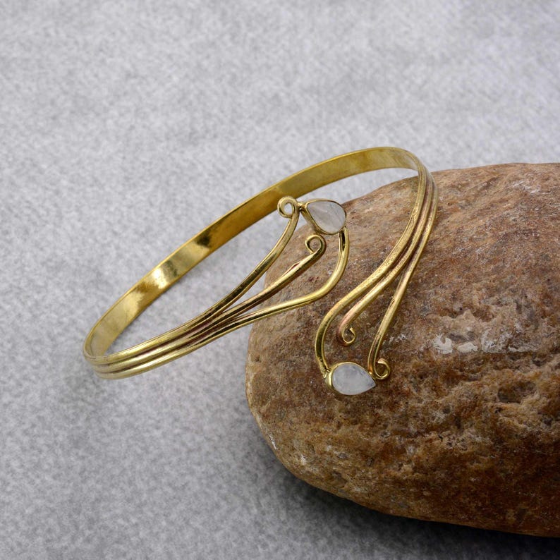 May include: A gold-tone bracelet with a delicate, flowing design and two white teardrop-shaped stones.