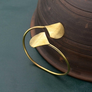May include: A gold-toned bangle bracelet with two leaf-shaped accents. The bracelet is open and has a simple design.