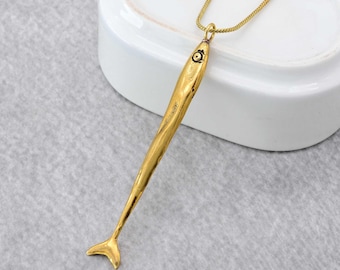 May include: A gold-toned fish pendant necklace with a chain. The pendant is long and thin, with a detailed fish design. The chain is delicate and has a lobster clasp.