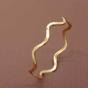 Può includere: Un braccialetto ondulato color oro. Il braccialetto è realizzato in metallo sottile e ha un design semplice ed elegante.