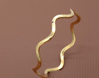 Puede incluir: Un brazalete ondulado de color dorado. El brazalete está hecho de un metal fino y tiene un diseño simple y elegante.
