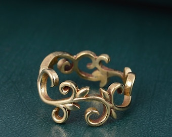 May include: A gold-toned ring with a delicate, intricate design resembling a vine with leaves. The ring is open and adjustable.