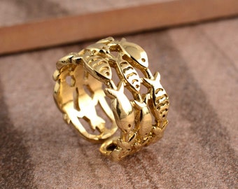 Puede incluir: Anillo de tono dorado con un diseño de varios peces entrelazados. El anillo es ajustable y se puede llevar en cualquier dedo.
