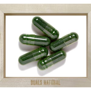 May include: Five dark green, translucent capsules filled with powder are arranged in a cluster. They are framed by a light-colored wooden border featuring the text "NYC" on the left, "1989" on the right, and "DUALS NATURAL" at the bottom.