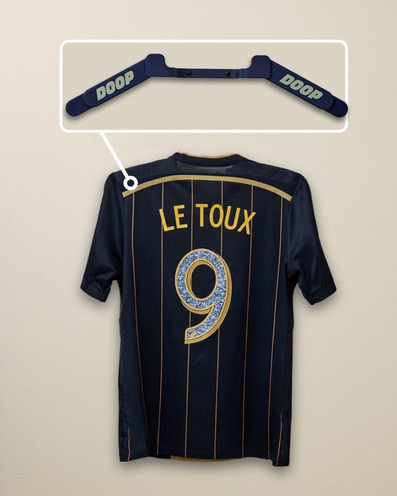 May include: Navy blue soccer jersey with gold vertical stripes and the name "LE TOUX" and the number "9" on the back. A blue hanger with the word "DOOP" is above the jersey.
