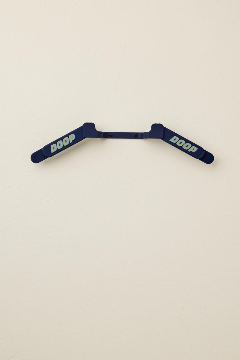 May include: A navy blue plastic hanger with the word "DOOP" printed in light blue on each end. The hanger is mounted on a white wall.