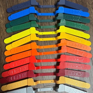 May include: A collection of colorful jersey racks in various shades, including blue, green, yellow, orange, red, and gray. Each rack has the word "JERSEY" or "RACKS" printed on it. The racks are arranged in a neat, organized display.