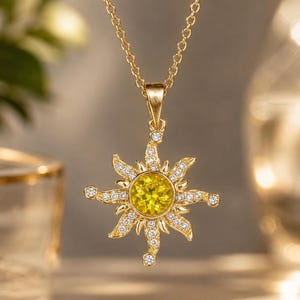 May include: A gold-toned necklace featuring a sun-shaped pendant. The center of the pendant holds a round, bright yellow gemstone, surrounded by rays encrusted with small, clear, sparkling stones. The pendant hangs from a delicate gold chain.