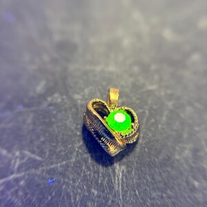 May include: A gold heart-shaped pendant with a green gemstone in the center.