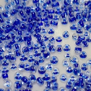 May include: A large quantity of small, round, glass beads in shades of blue and clear. The beads have a hole in the center for stringing.