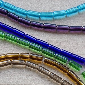 May include: Assortment of glass beads in various colors, including brown, blue, green, and purple. The beads are arranged in rows and are all the same size and shape.