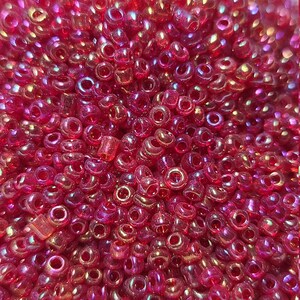 May include: Close-up of a pile of small, translucent, red-pink beads. The beads have a hole through the center and reflect light, creating a shimmering effect. The beads are scattered, filling the frame.