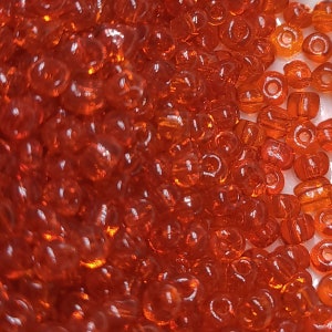 May include: A close-up of a pile of small, round, orange glass beads. The beads are translucent and have a slight shimmer to them.