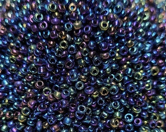 May include: A large pile of iridescent blue, purple, and green seed beads. The beads are small and round, and they have a metallic sheen.