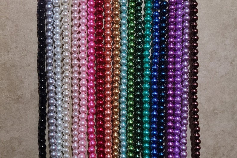 May include: A collection of beaded strands in a variety of colors, including black, silver, white, pink, red, gold, green, blue, purple, and brown. The beads are uniform in size and appear to be pearls, creating a visually appealing display.