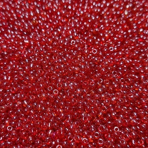 May include: A close-up image of a large quantity of small, red, round glass beads. The beads are arranged in a random pattern and have a slight iridescent sheen.