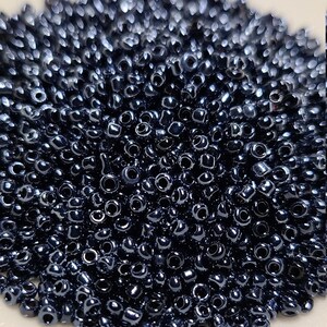 May include: A pile of dark blue seed beads. The beads are small and round, with a metallic sheen.