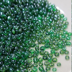 May include: A pile of small, round, green glass beads with a shiny, iridescent finish.