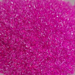 May include: A large pile of small, round, translucent pink beads. The beads are shiny and have a slight iridescent quality.