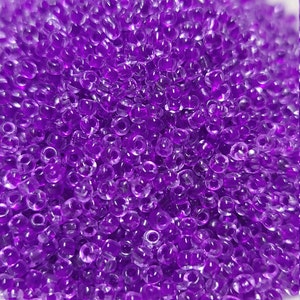 May include: A large pile of small, round, transparent purple beads. The beads are translucent and have a slight shimmer.