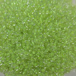 May include: A large pile of small, clear, green glass beads. The beads are round and have a slight iridescent sheen.