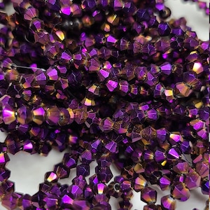 May include: A close-up of a pile of iridescent purple and gold faceted glass beads. The beads are small and have a shiny finish.