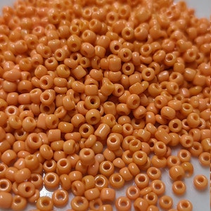 May include: A pile of small, round, orange beads. The beads are made of glass and have a smooth, shiny finish.