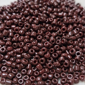 May include: A large pile of small, dark brown seed beads. The beads are round with a hole in the center.